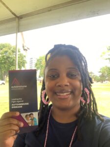 A volunteer is smiling and holding an Autoimmune Association brochure.
